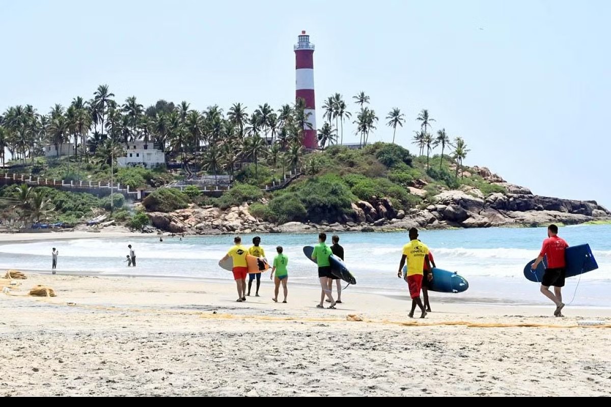 Beachgoers along the water with the lighthouse in the distance